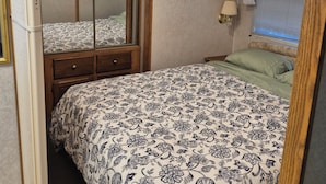 Ein Schlafzimmer mit einem Bett, einem Schminktisch, einem Spiegel, einem Nachttisch, einer Lampe und einem Fenster mit Jalousien.