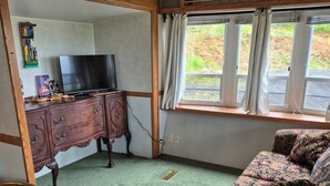 Ein Zimmer mit Fernseher auf einem Holzschrank, einer floral gepolsterten Couch und einem Fenster mit Vorhängen.