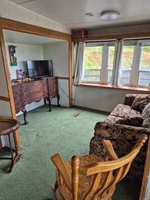 A room with a television on a wooden cabinet, a sofa with floral upholstery, and a window with curtains. - Welcome to Norma's Nest overlooking St Mary's Bay, 12kms to Digby N.S. (Digby)