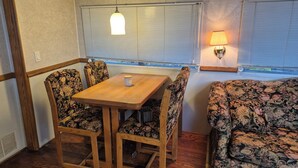 Ein gemütliches Wohnmobil-Interieur mit Holztisch, Stühlen mit Blumenmuster, einer Sitzecke und einer Hängelampe.