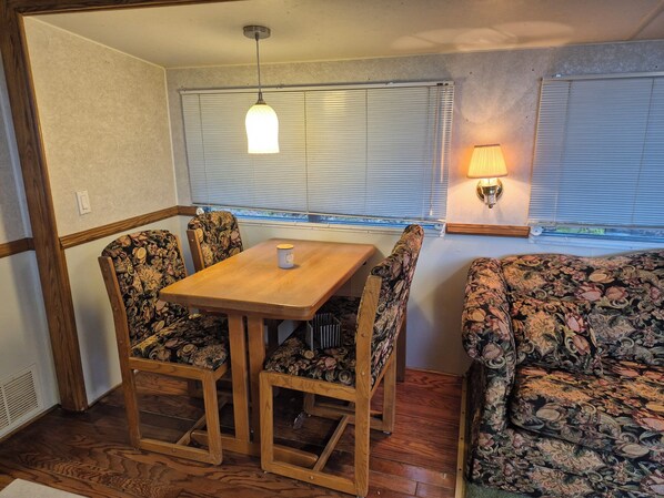 A cozy RV interior with a wooden table, floral-patterned chairs, a sofa, and a hanging light fixture.