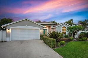 Ein Wohnhaus mit Garage und Gartenanlage, bewölkter Himmel bei Sonnenuntergang.
