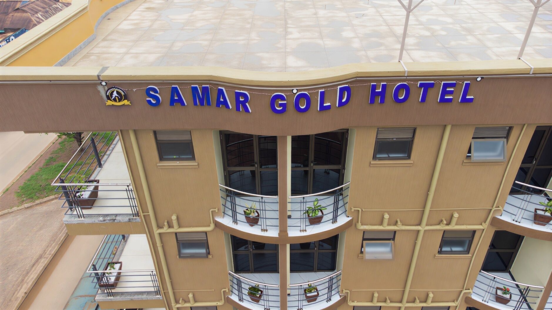 Um hotel de vários andares com varandas, um letreiro com a inscrição 'SAMAR GOLD HOTEL' e um logotipo acima do letreiro.
