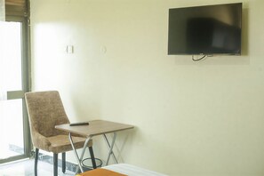 Una habitación con una televisión montada en la pared, una silla, una mesita y un ventanal.