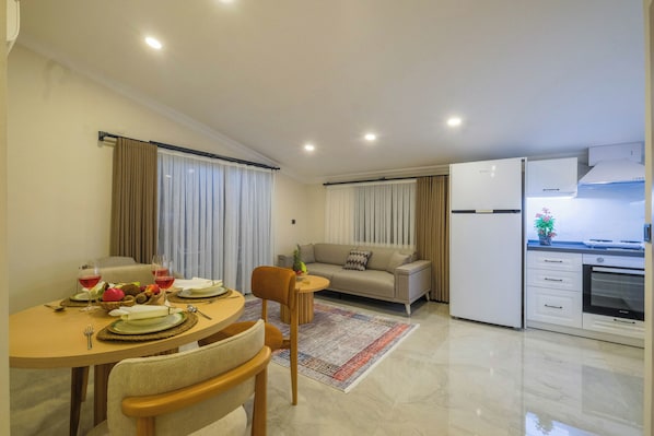 A modern living space with a dining area, a sofa, a kitchen, and a refrigerator. - Viranlar Residance (Fethiye)