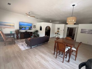 A spacious living room with a flat-screen TV, a sofa, a dining table with chairs, and a ceiling fan.