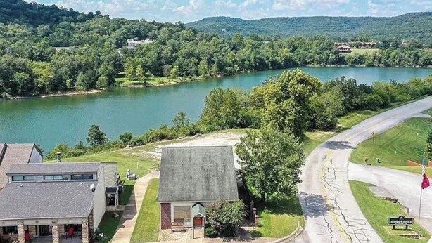Um imóvel à beira do lago, com uma estrada serpenteando ao redor de um edifício, rodeado por vegetação e colinas.