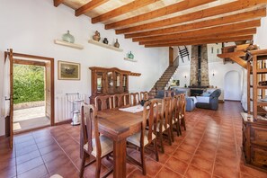 A spacious dining area with a wooden table and chairs, a kitchen with a chimney, and a staircase leading to an upper level. - Country Villa With Garden for 6 (Pollença)