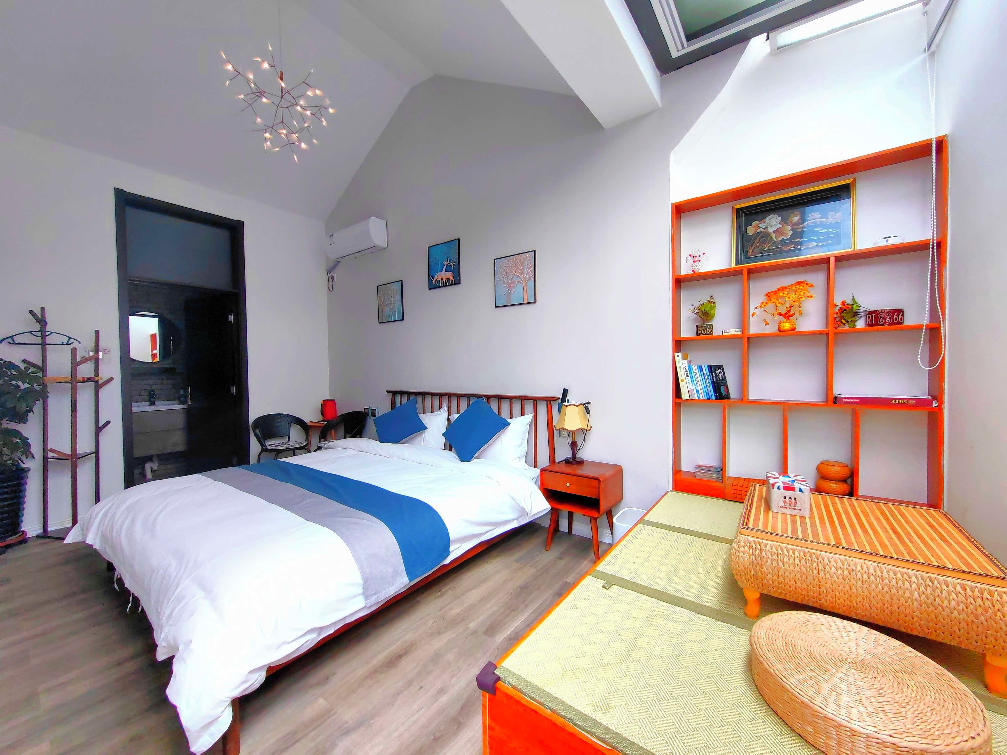 Un dormitorio moderno con cama, mesita de noche y un pequeño sofá. Hay una estantería con objetos decorativos y un estante montado en la pared.