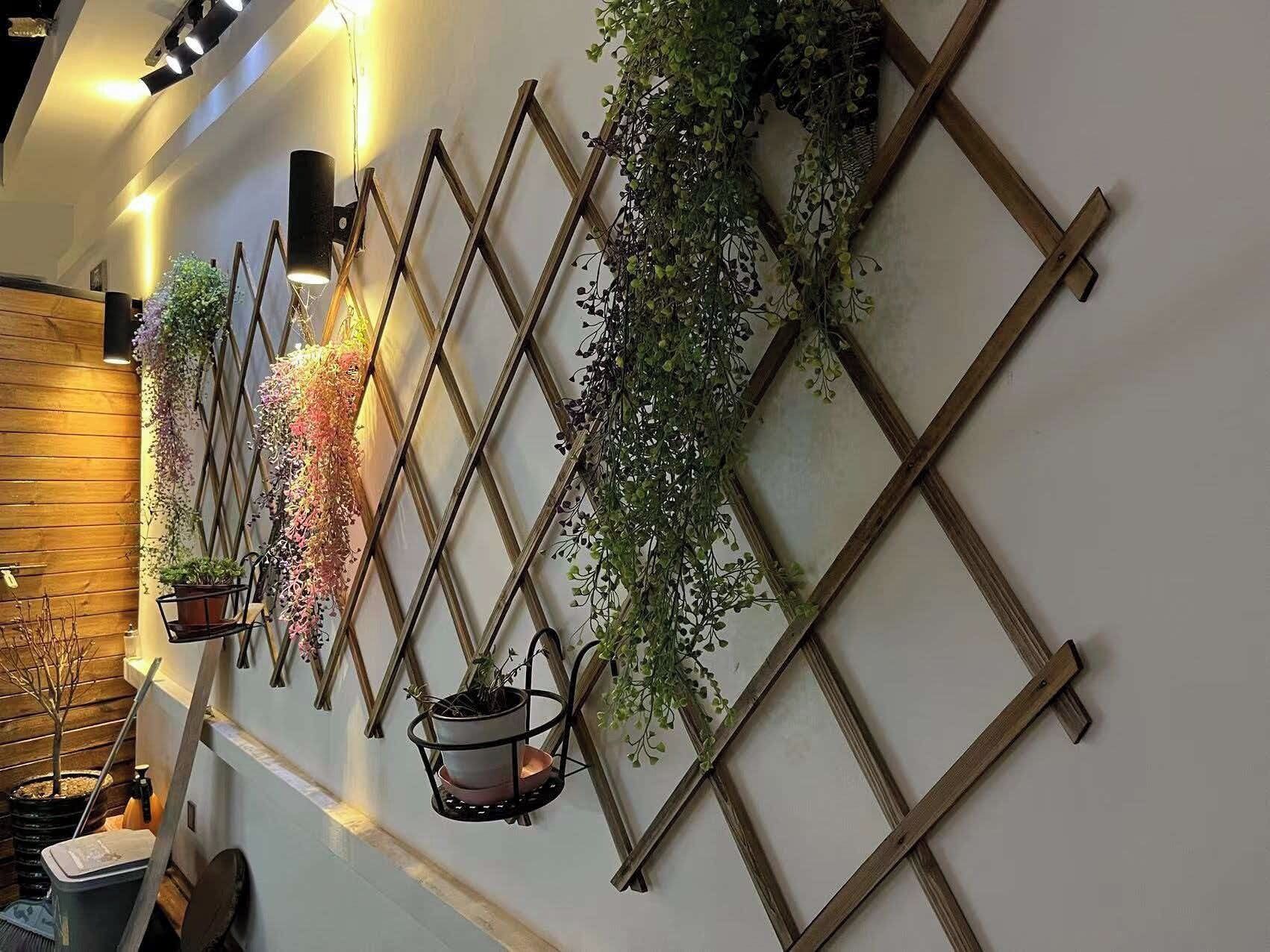 A wall with a wooden lattice design, adorned with various potted plants and hanging baskets.