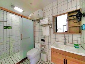 Baño con inodoro, lavabo y espejo. Hay una señal de precaución en la pared y un perchero para toallas.