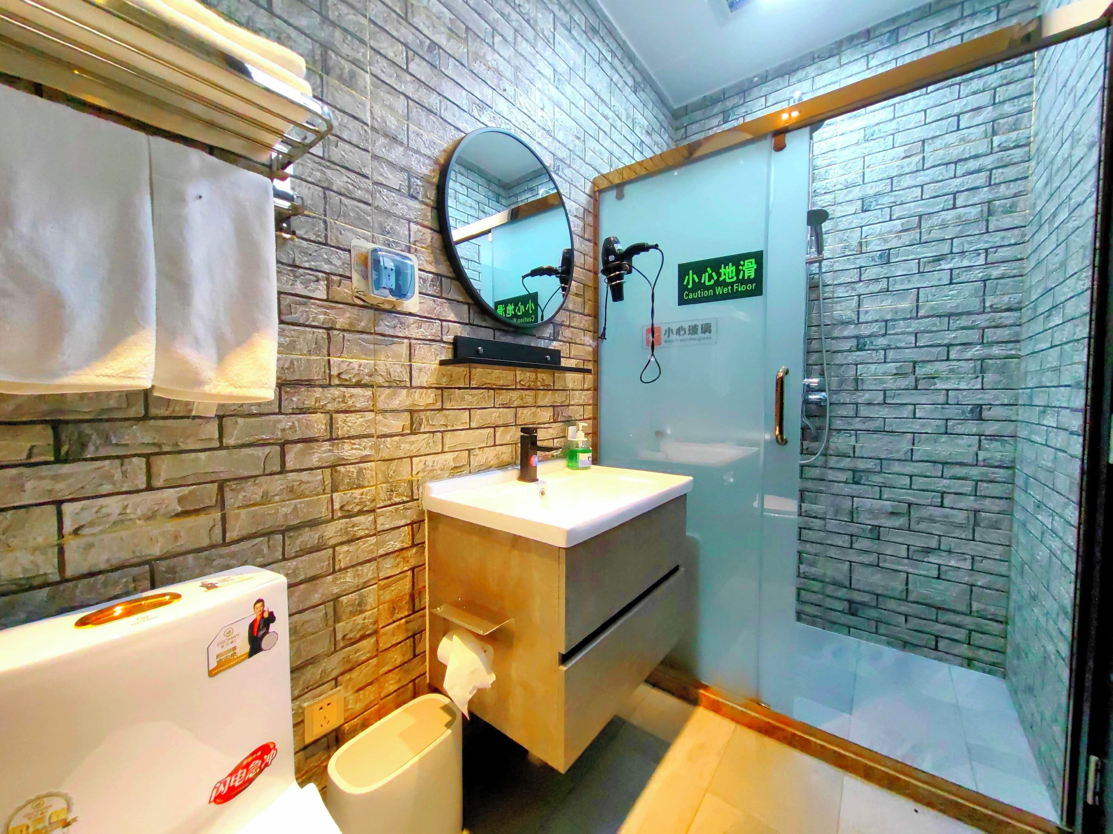 Un baño con pared de ladrillo, un lavabo, un espejo, un inodoro y una cabina de ducha de vidrio.