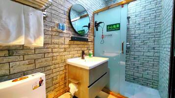 Un baño con pared de ladrillo, un lavabo, un espejo, un inodoro y una cabina de ducha de vidrio.
