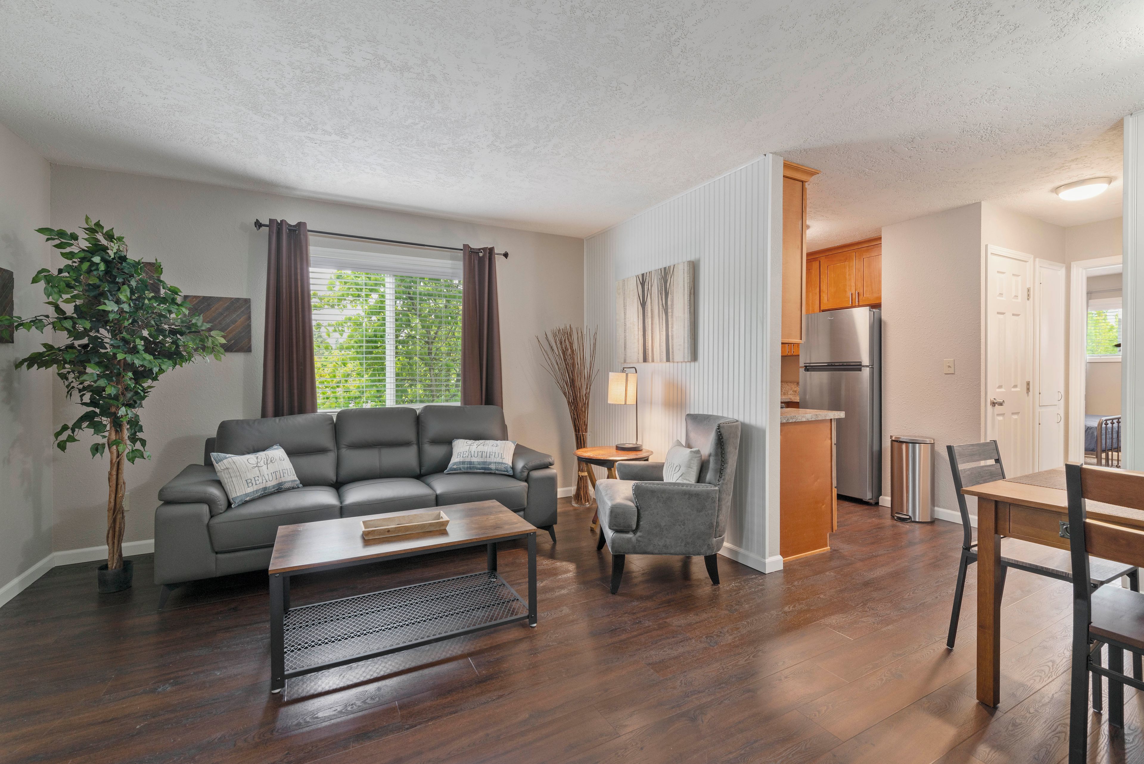 A modern living room with a sofa, armchair, coffee table, and a dining area with a table and chairs.
