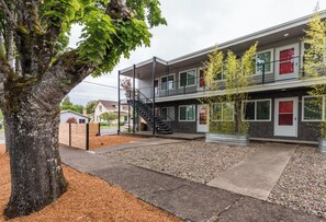 Un edificio de dos plantas con un espacio exterior techado, una escalera y un árbol en primer plano.