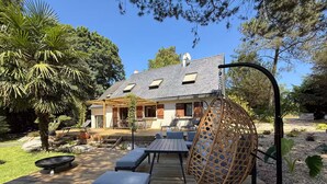 A wooden deck with outdoor furniture, a hanging chair, and a house in the background. - Vrbo Property (Molac)