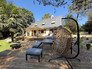 A wooden deck with outdoor furniture, a hanging chair, and a house in the background. - Vrbo Property (Molac)
