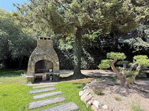 A stone-built outdoor fireplace surrounded by a well-maintained garden with a stone pathway leading to it. - Large house with a private pond (Molac)