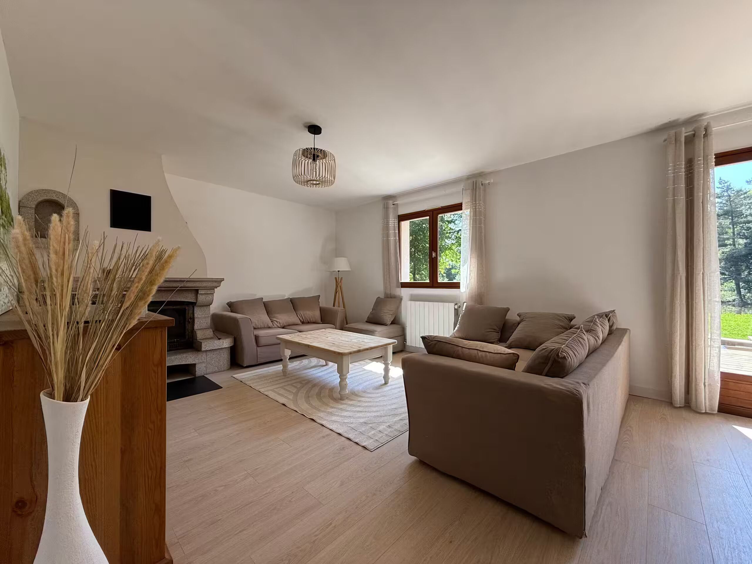 A spacious living room with a fireplace, two sofas, a coffee table, and a large window with curtains.