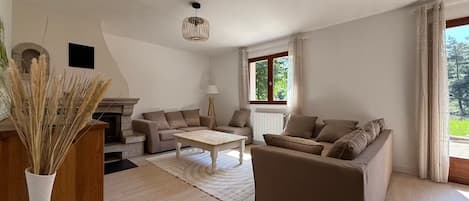 A spacious living room with a fireplace, two sofas, a coffee table, and a large window with curtains.