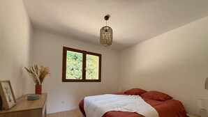 A bedroom with a bed, a window, a desk, and a hanging light fixture. - Vrbo Property (Molac)