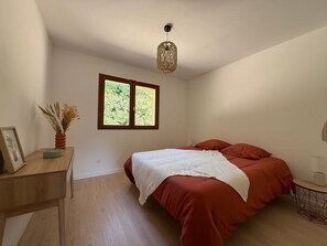 A bedroom with a bed, a window, a desk, and a hanging light fixture. - Vrbo Property (Molac)