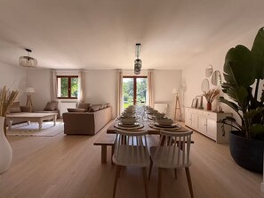 A spacious living room with a long dining table set for a meal, a sofa, and a coffee table. - Large house with a private pond (Molac)