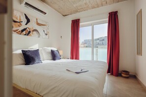 Ein Hotelzimmer mit einem Bett, einem Fenster mit roten Vorhängen, Blick auf die Stadt und einem Deckenventilator.