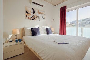 Una habitació d'hotel amb un llit gran, dues làmpades al costat del llit, una tauleta de nit, un quadre a la paret i vistes per la finestra.