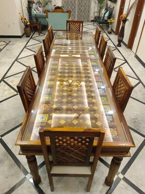 Une longue table à manger avec un plateau en verre et des chaises en bois, entourée d’un sol à motifs.