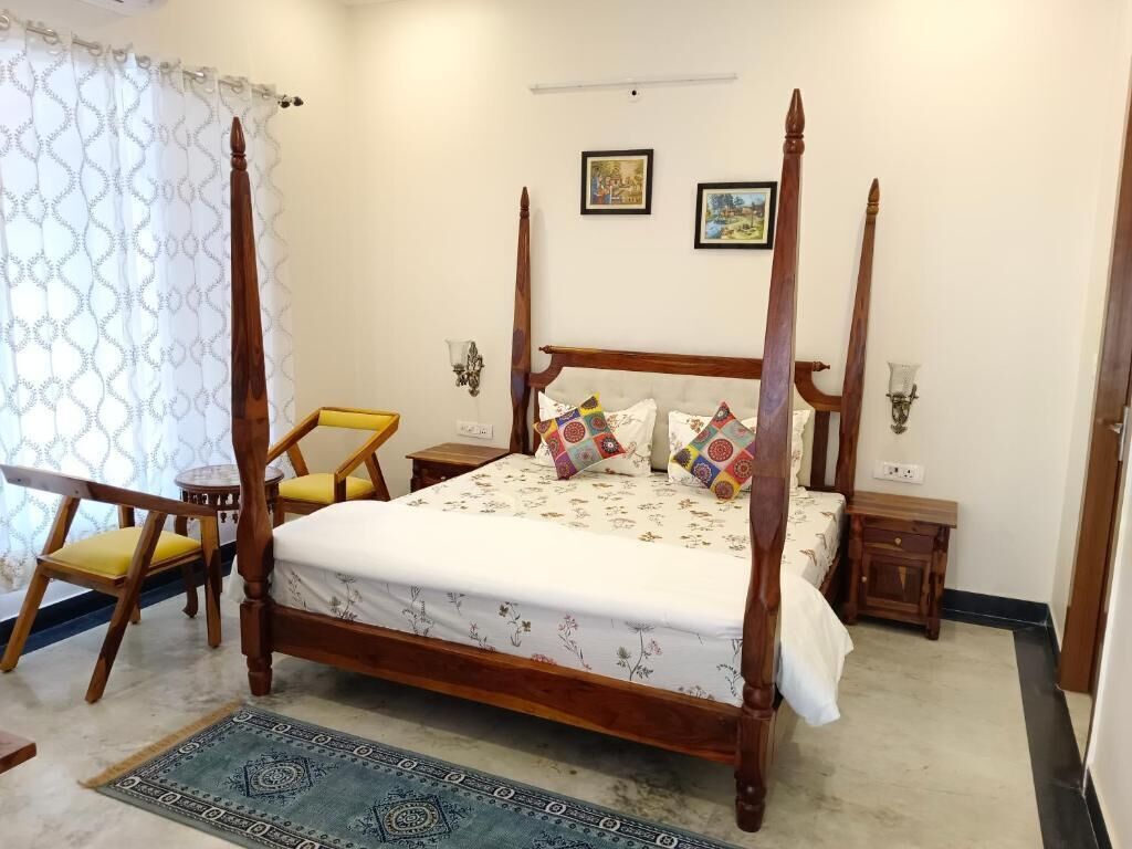 A four-poster bed with a floral bedspread, a small round table, and a chair with yellow cushions.