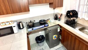 A compact kitchen with wooden cabinets, a microwave, a gas stove, and a refrigerator. - Modern two bedroom apartment in Central Kisumu. Wifi and secure parking (Kisumu)