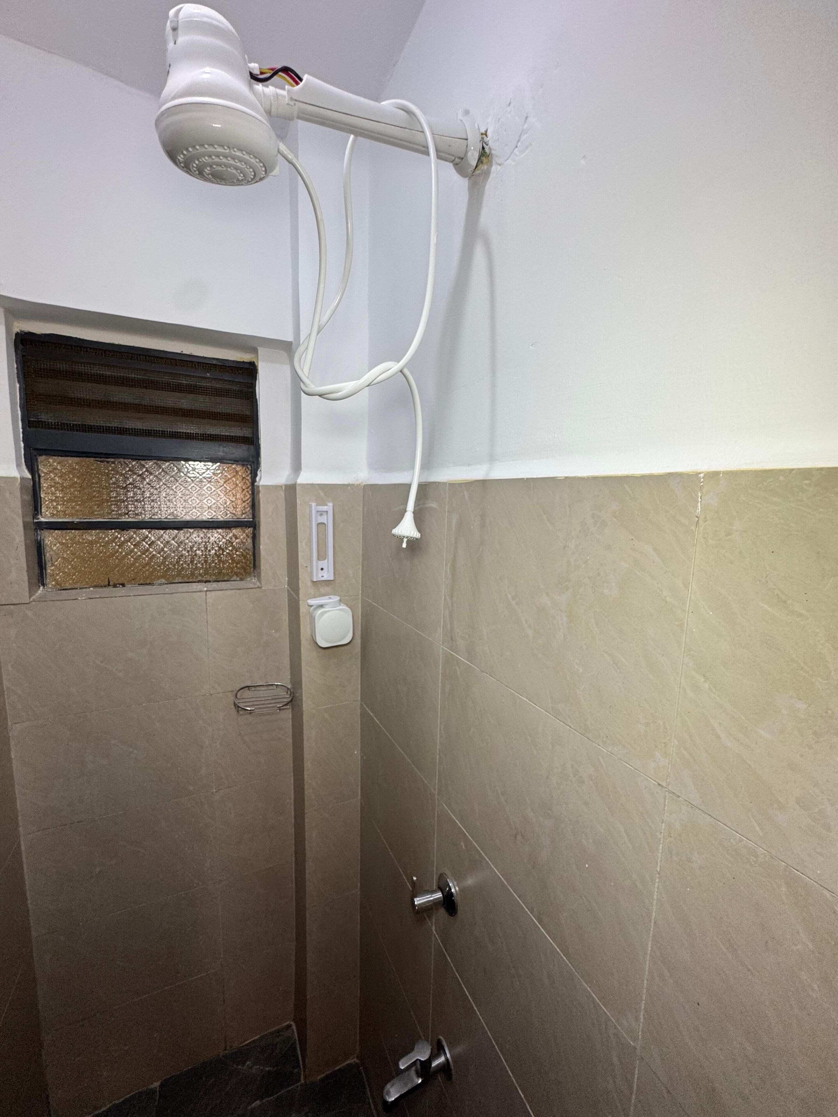 Een badkamer met een douche, een raam met decoratief rooster en een handdoekhouder.