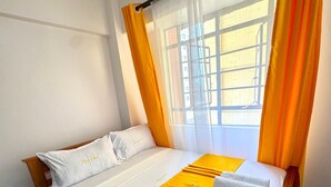 A hotel room with a bed, a window with curtains, a fluffy rug, and slippers. - Modern two bedroom apartment in Central Kisumu. Wifi and secure parking (Kisumu)