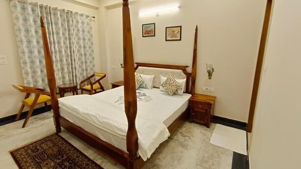 A four-poster bed with a white bedspread, a wooden headboard, and two bedside tables with lamps. - Gupta Vilas - A Boutique Homestay - Standard King Room 4 (Agra)