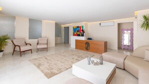 A modern living room with a white sofa, two armchairs, a coffee table, and a reception desk with a colorful artwork. - Seven Stays Centric West  (Giza Governorate)