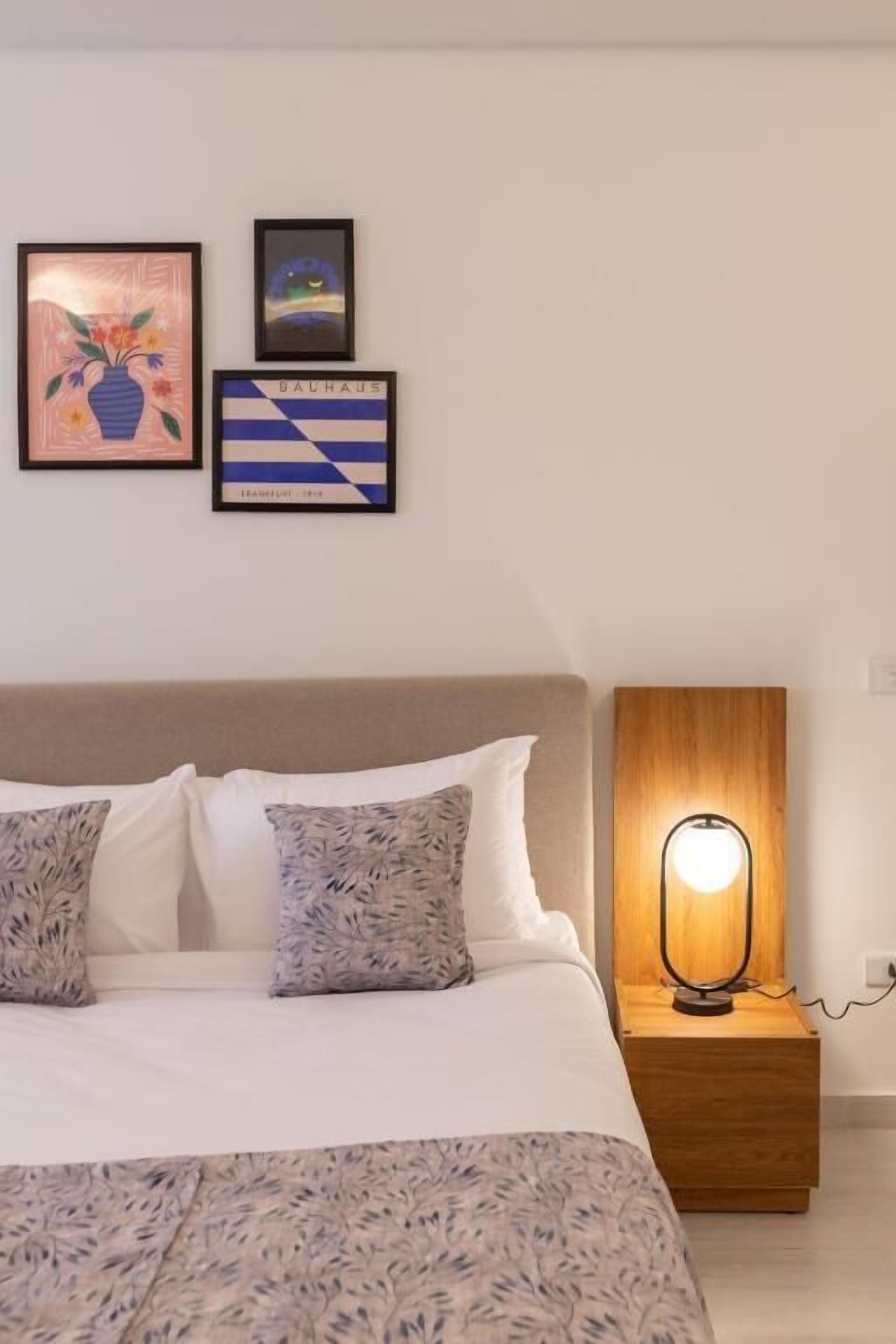 Cama bem arrumada com colcha estampada, luminária de cabeceira e duas obras de arte emolduradas na parede.