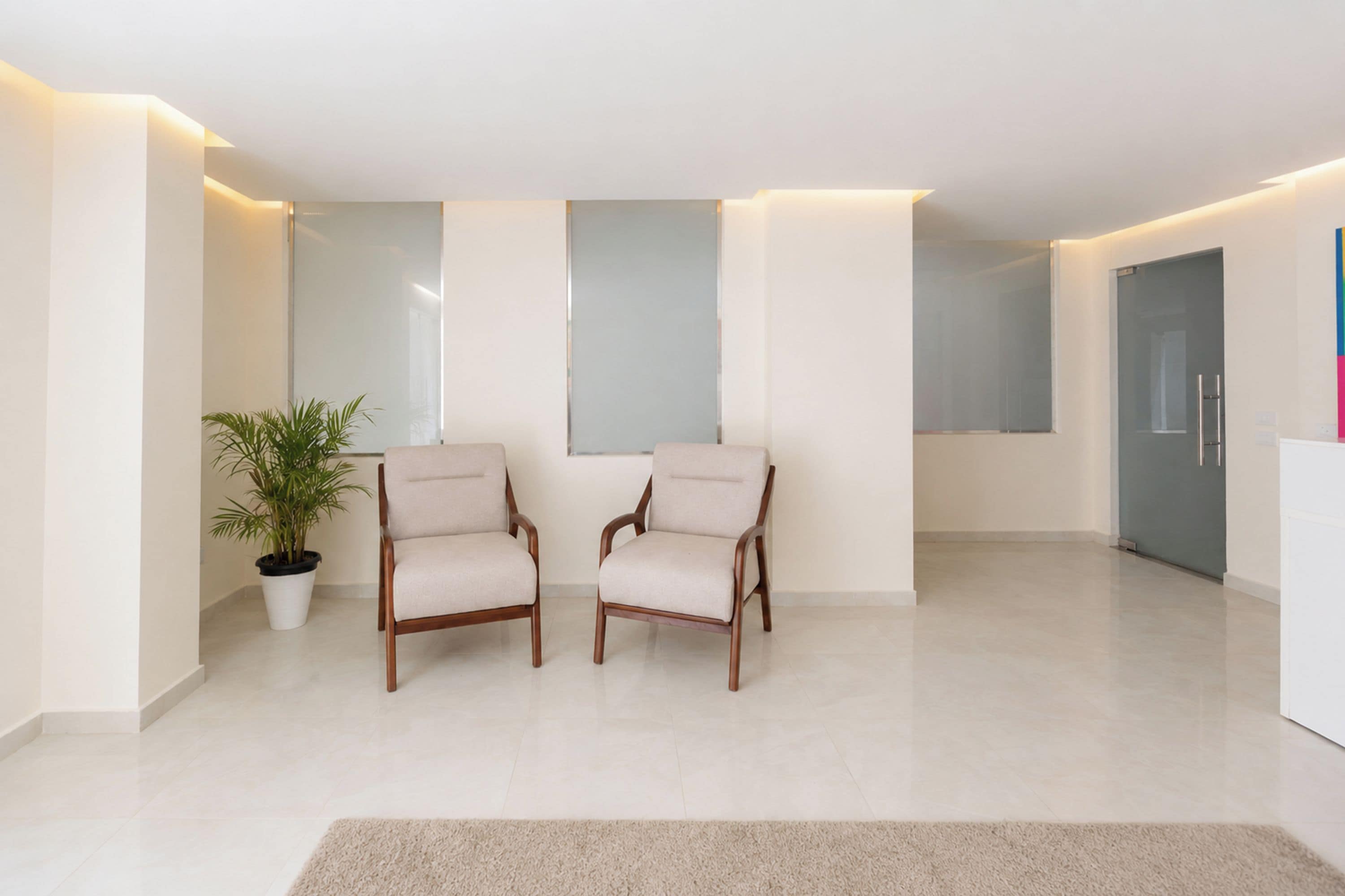 Una habitación moderna y minimalista con dos sillas de madera, una planta en maceta y un espejo grande en la pared.