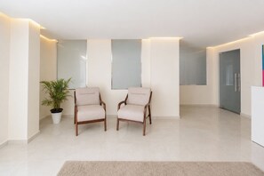 A modern, minimalist room with two wooden chairs, a potted plant, and a large mirror on the wall.