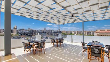 Un área de estar al aire libre con mesas y sillas, vista del paisaje urbano y techo con diseño.
