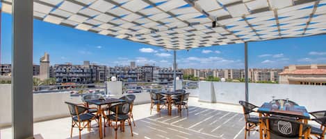 Un espace extérieur aménagé avec des tables et des chaises, une vue sur le paysage urbain et un plafond décoré de motifs.