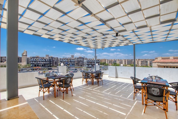 Un área de estar al aire libre con mesas y sillas, vista del paisaje urbano y techo con diseño.