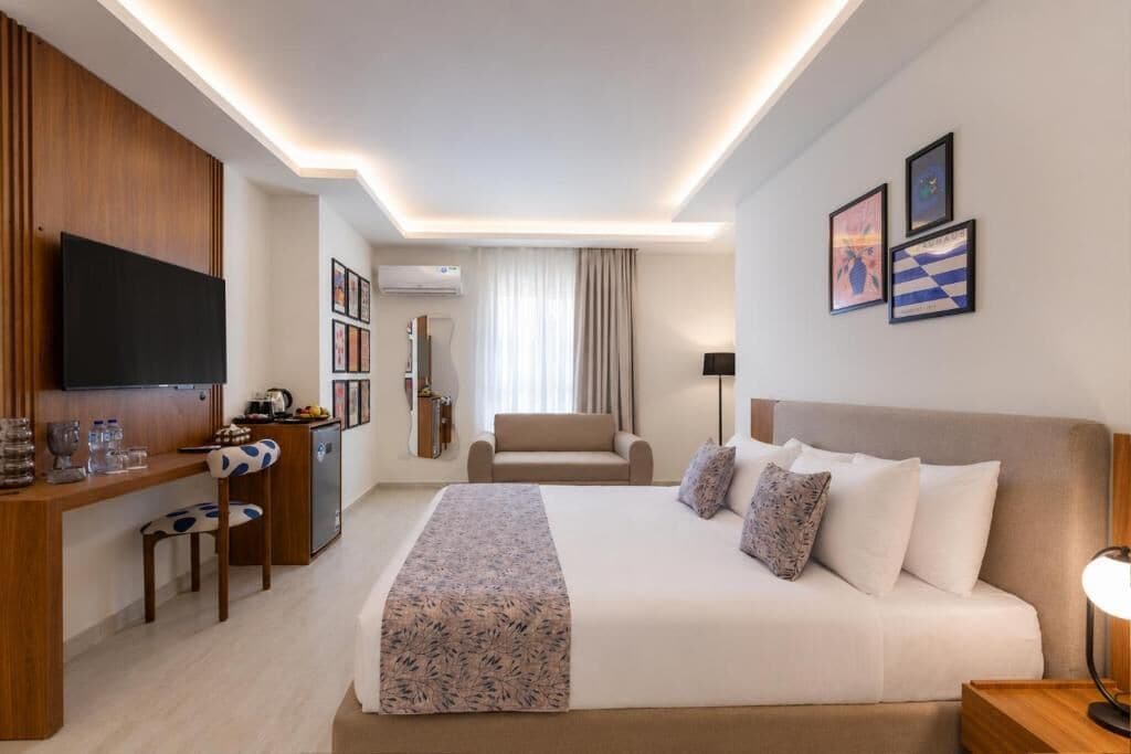 A hotel room with a bed, a desk with a chair, a television, and artwork on the walls.