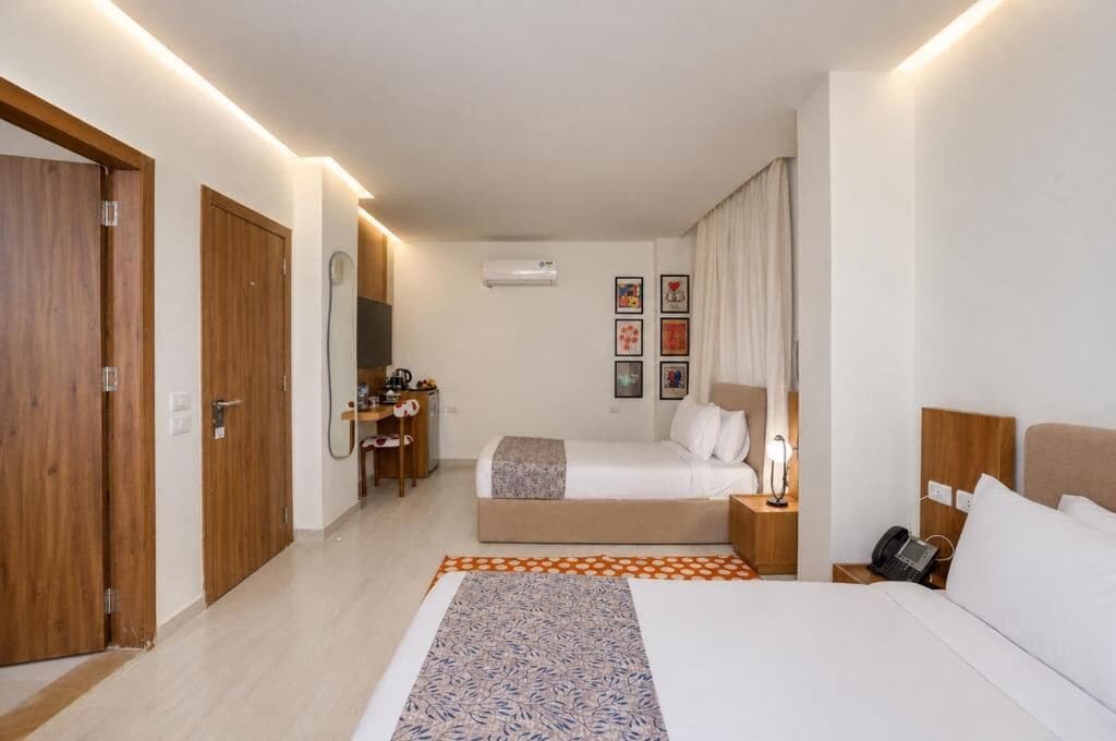 A hotel room with a bed, bedside table, lamp, and a desk with a chair.