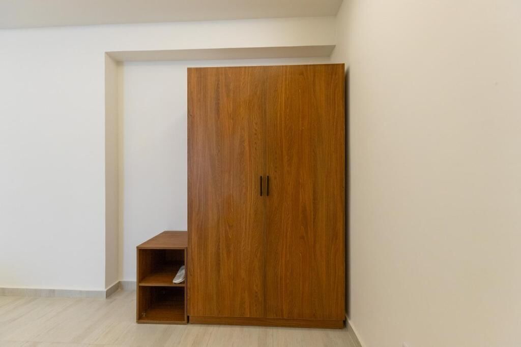 A room with a wooden wardrobe, a small wooden shelf, and a white wall.