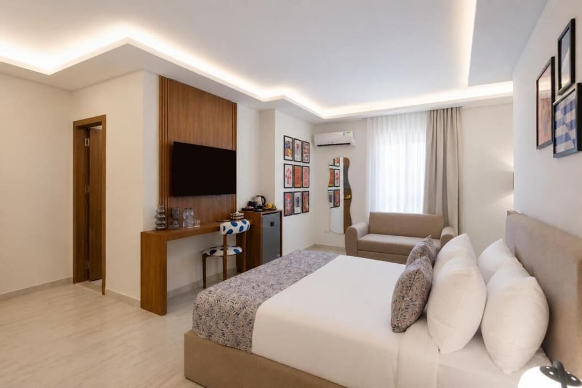 A hotel room with a bed, a desk, a chair, and a TV mounted on the wall.