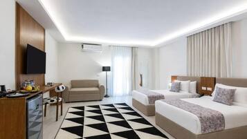 Quarto de hotel com duas camas, uma escrivaninha com computador, uma cadeira, televisão e uma janela grande com cortinas.