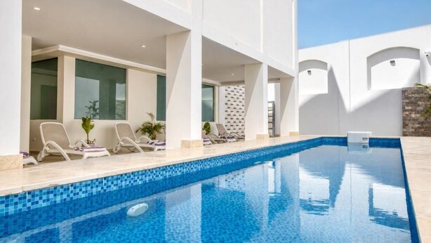 A swimming pool with lounge chairs and a tiled deck area. - Seven Stays Centric West  (Giza Governorate)
