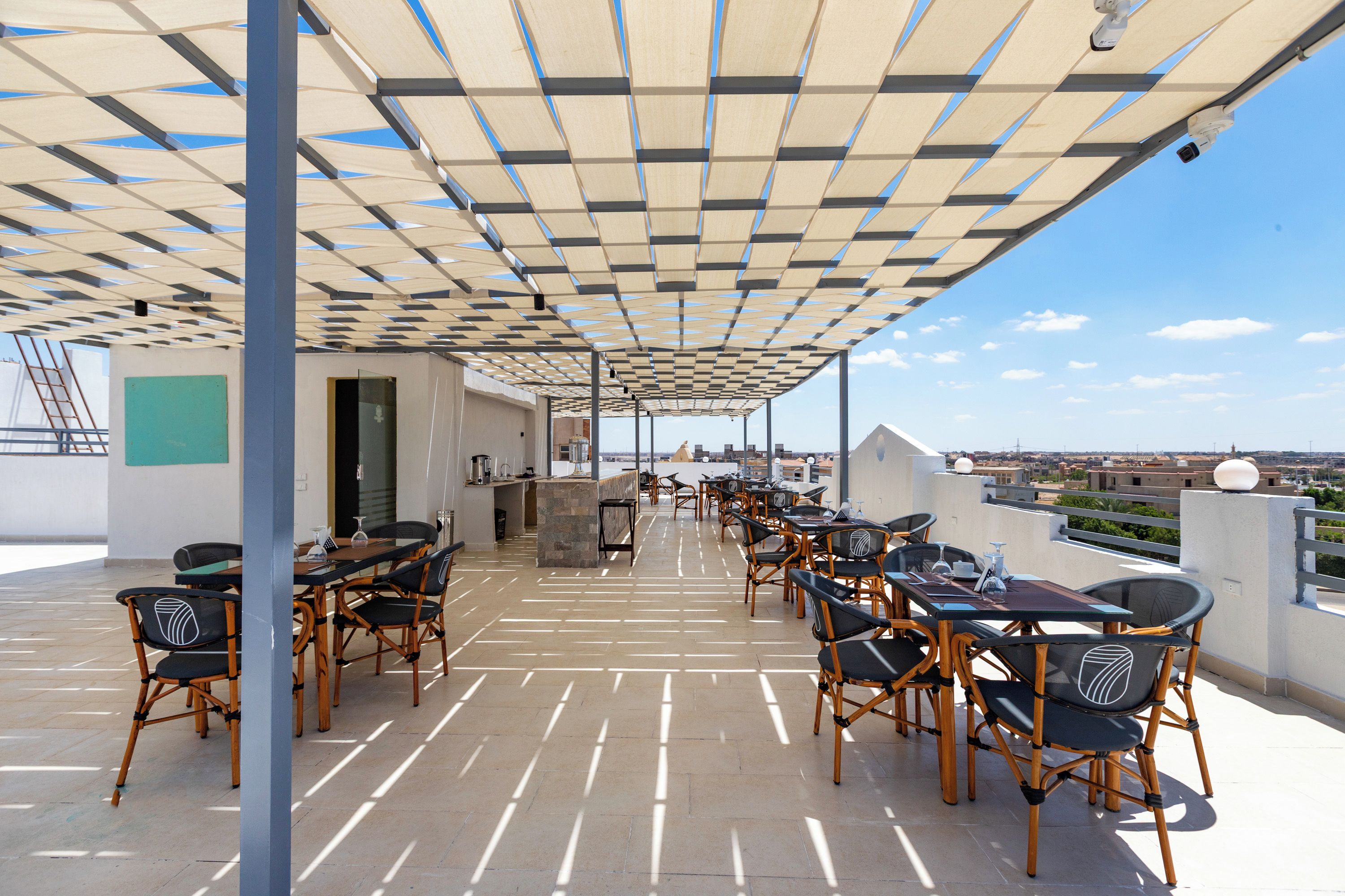 An outdoor terrace with a checkered shade structure, multiple dining tables, and chairs.
