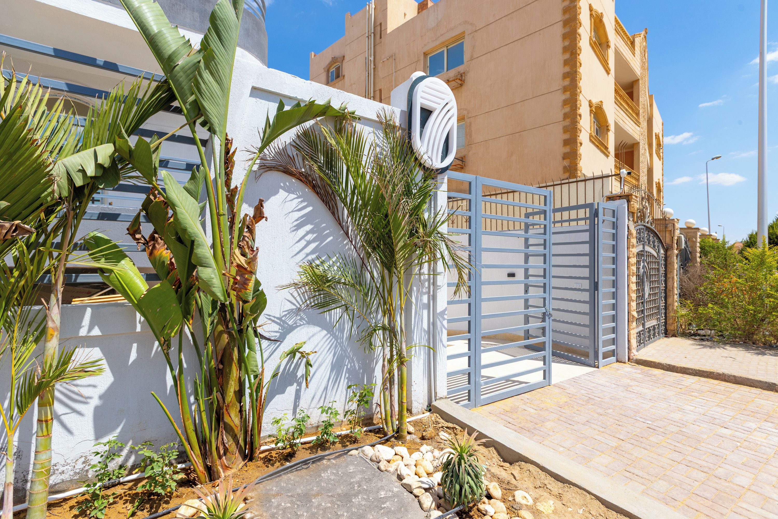 A gated entrance with a white wall and tropical plants.